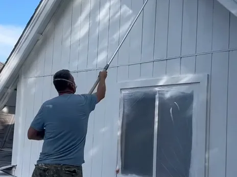 JTM Remodeling painter rolling fresh paint onto a gable wall with the window masked off