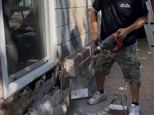 JTM Remodeling crew member removing deteriorated masonry at the base of an exterior wall